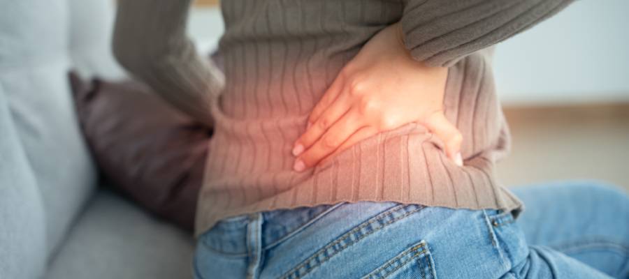 Belini tutarak ağrı hisseden, kot pantolon ve kazak giymiş bir kişi; bel fıtığına bağlı rahatsızlık hissini ifade ediyor.