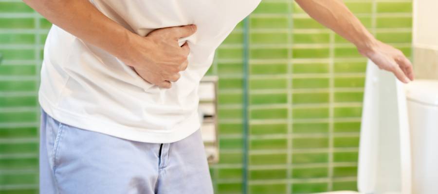 Karın ağrısı çeken ve tuvalete tutunarak eğilmiş bir kişi. İshal veya ani tuvalet ihtiyacı nedeniyle rahatsızlık yaşıyor gibi görünüyor.