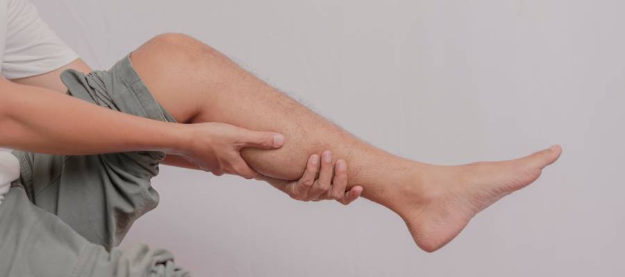 Bir kişi, baldır bölgesinde kas spazmı veya ağrı hissederek bacağını iki eliyle tutuyor.