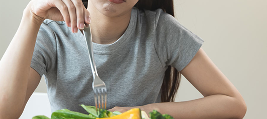 Gri tişört giymiş bir kadın, önündeki salataya çatal batırmış şekilde isteksizce bakıyor.
