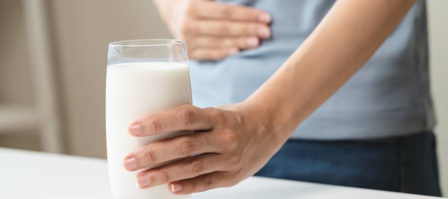 Laktoz intoleransı yaşayan bir kişi, elinde bir bardak süt tutarken diğer eliyle karnını tutuyor.