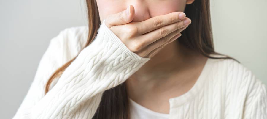 Ağzını eliyle kapatan genç kadın; mide bulantısı veya kusma hissi yaşayan biri.