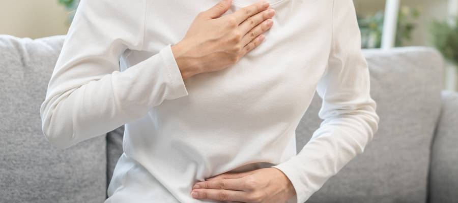 Göğüs ve karın bölgesinde yanma hissi yaşayan bir kişi; mide yanması (heartburn) semptomlarını gösteren kadın.