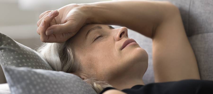 Başını yastığa yaslamış ve alnını tutan, migren ağrısı çeken orta yaşlı bir kadın.