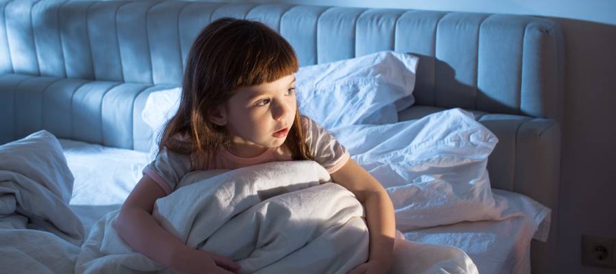 Gece terörü yaşayan küçük bir kız çocuğu yatağında uyanmış halde korku içinde etrafa bakıyor.