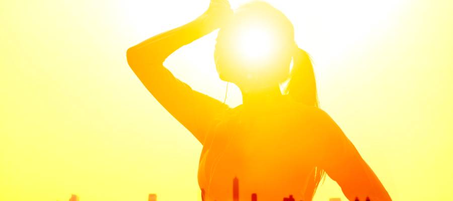 Güneş altında başını tutan bir kadın silueti; yoğun güneş ışığı ve sıcak hava güneş çarpmasını simgeliyor.