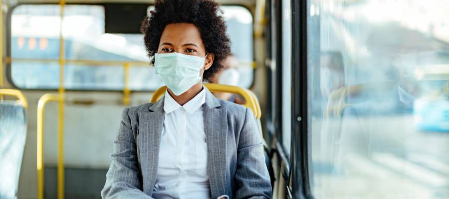 Maske takan ve toplu taşımada seyahat eden, resmi giyimli bir kadın. Pandemi veya ani salgın döneminde toplu taşıma önlemlerini temsil eden bir sahne.