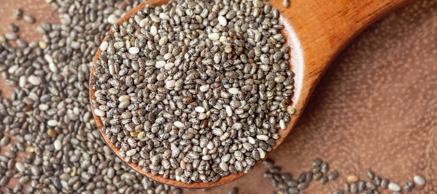 Bir tahta kaşık üzerinde ve etrafına dağılmış halde görünen siyah-beyaz renkli chia tohumları yakın plan çekimde.