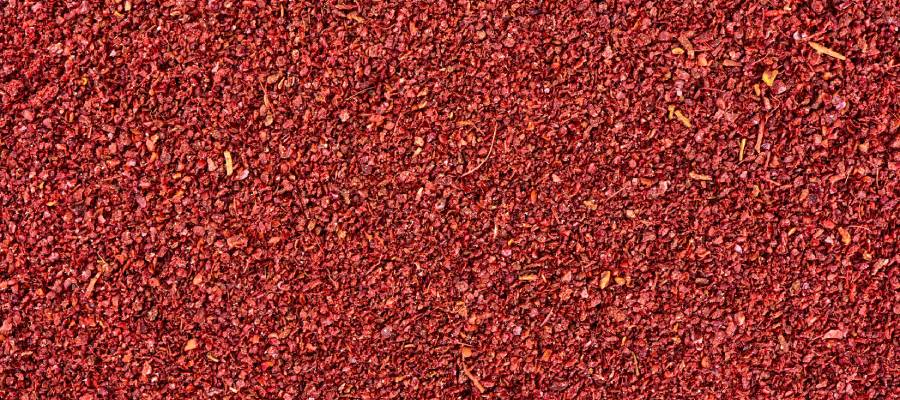 Canlı kırmızı renkteki öğütülmüş sumak baharatının dokulu ve tanecikli yüzeyinin yakın çekim fotoğrafı.