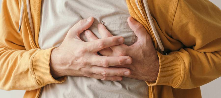 Göğsünü tutan bir kişi; göğüs ağrısı yaşayan bir erkek, sarı kapüşonlu ceket giymiş.