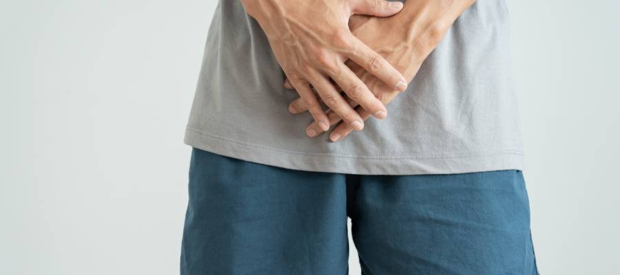 Ellerini kasık bölgesine koymuş bir erkek, cinsel sağlıkla ilgili rahatsızlık veya utanç ifadesi.