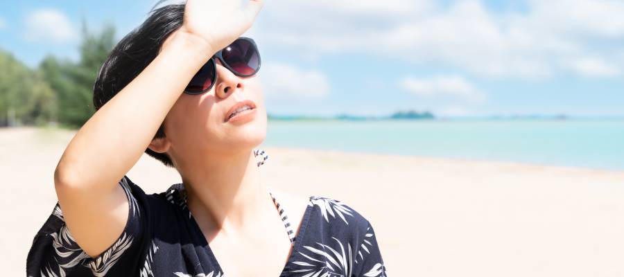 Güneşli bir plajda başını güneşten korumaya çalışan güneş gözlüklü kadın.