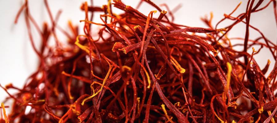 Koyu kırmızı safran iplikçiklerinin birbirine karışmış halde durduğu detaylı bir makro fotoğraf. Ön plandaki net görüntüde, bazı tellerin daha açık sarı ve turuncu renkteki uçları belirgin bir şekilde görülüyor.