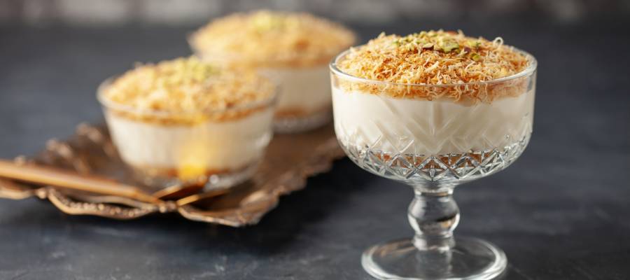 Ön planda cam kâsede kadayıflı muhallebi, arka planda tepside benzer sunumlarla geleneksel bir tatlı servisi.