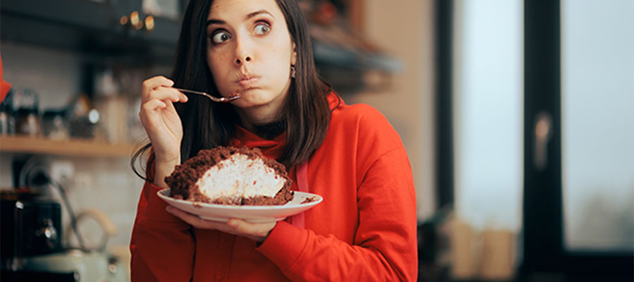 Kırmızı kapüşonlu bir kadın, büyük bir dilim pastayı hızlıca yerken şaşkın ve suçlu bir ifadeyle etrafına bakıyor.